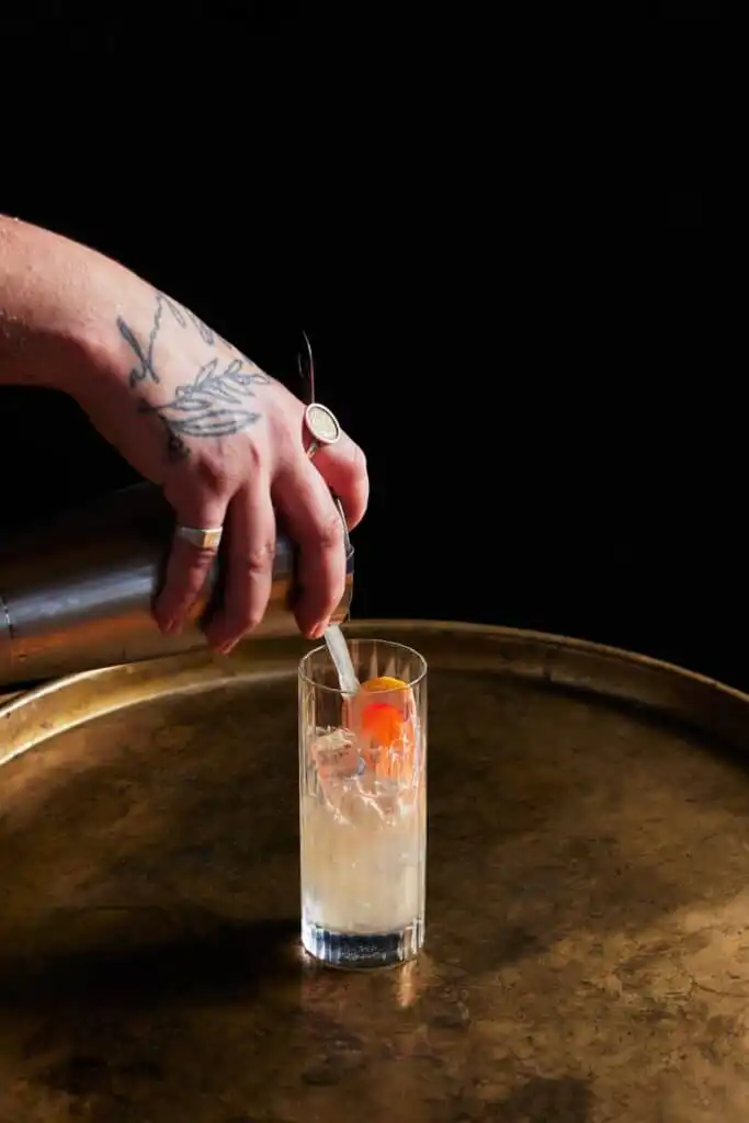 A bartender garnishing a cocktail on a brass tray